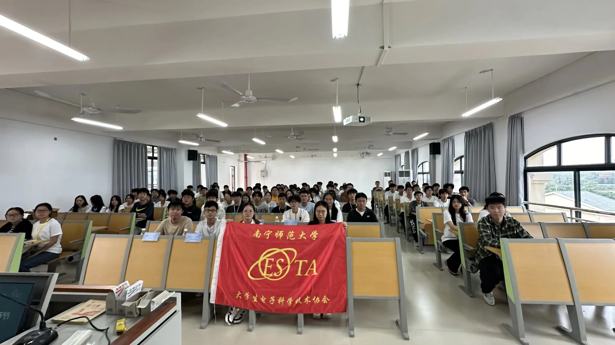 全体大会教室内，参与者与社团旗帜合影